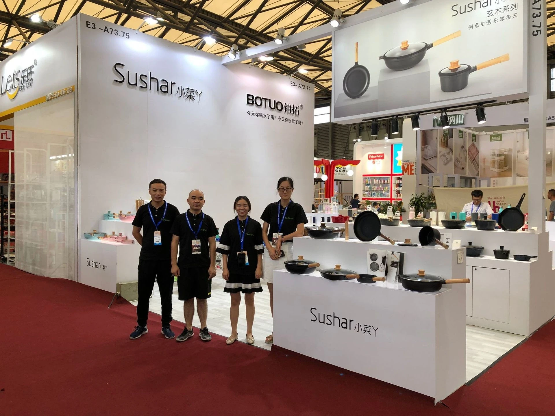 Four team members at the Sushar Xiaocaiya exhibition stand with cookware on display