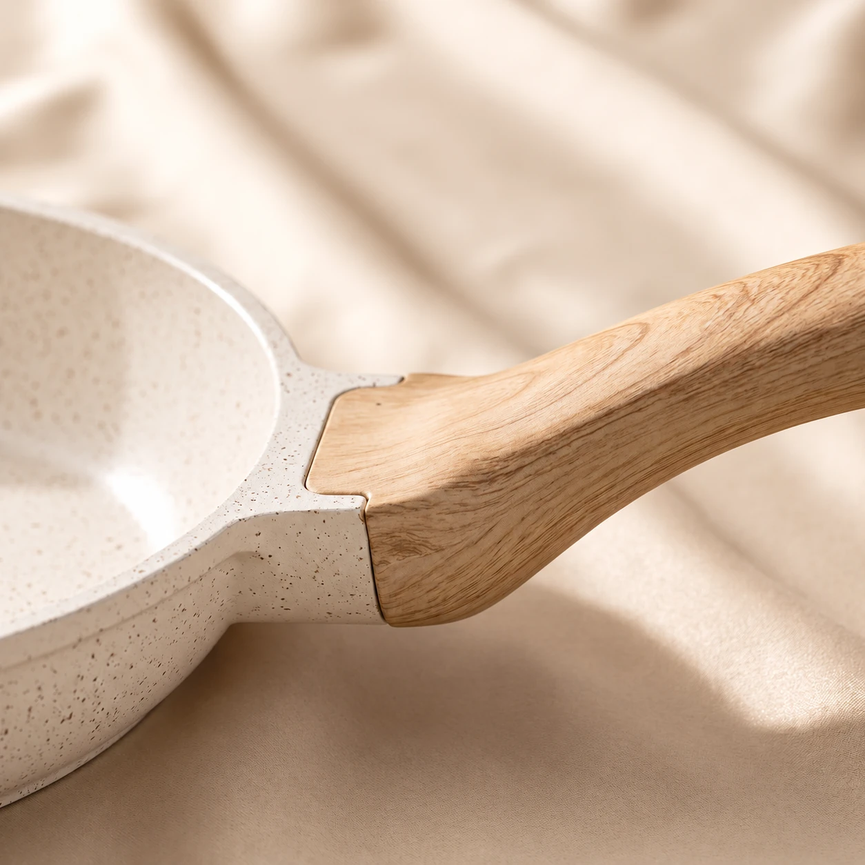 Close-up of an ivory speckled pan and its wood-look handle joint on cream linen
